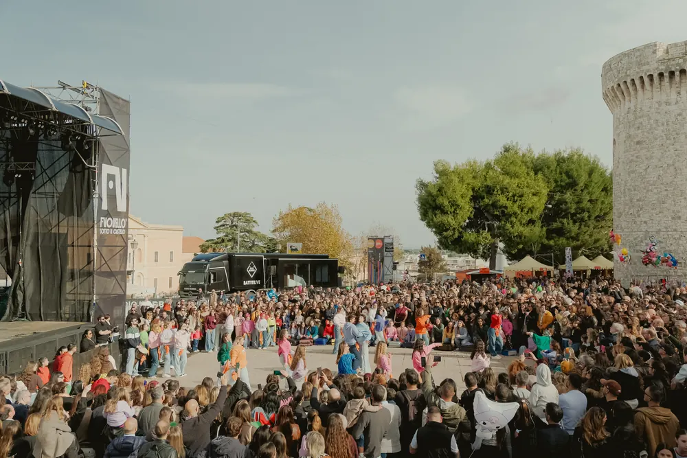 La piazza piena di gente di giorno, davanti al palco e al castello